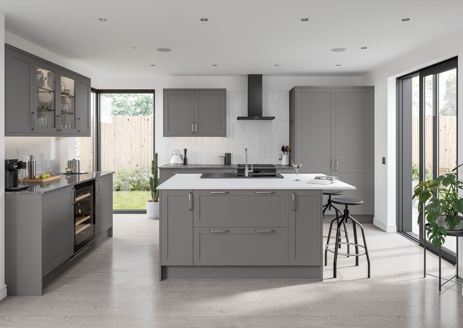 Skye Shaker Kitchen in dust grey is shown in this kitchen design. White worktops and dust grey cabinets create a modern kitchen feel. A mix of tall cabinets and larders along with a kitchen island, creates an impressive space. Wall to ceiling windows make the kitchen bright and airy, there are also smart features like a coffee machine, designer bar stools and cooker with hood in matte black.